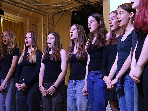 Ein Chor aus jungen Frauen steht auf einer Bühne und singt.