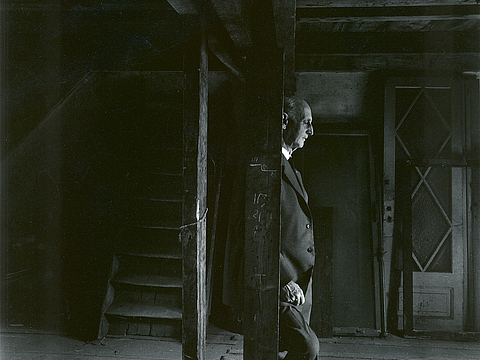 Ein Mann steht auf einem leeren Dachboden und lehnt an einer Holzsäule.